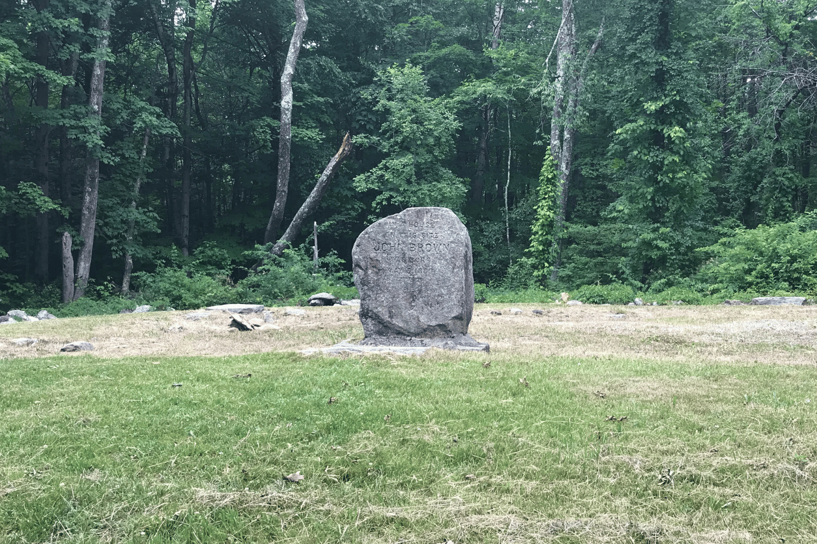 John Brown birthplace marker in Torrington, Connecticut, standing in a grassy clearing at the edge of the woods.